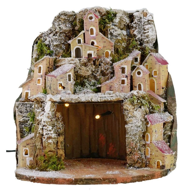 Illuminated snow-covered nativity scene with village and cave